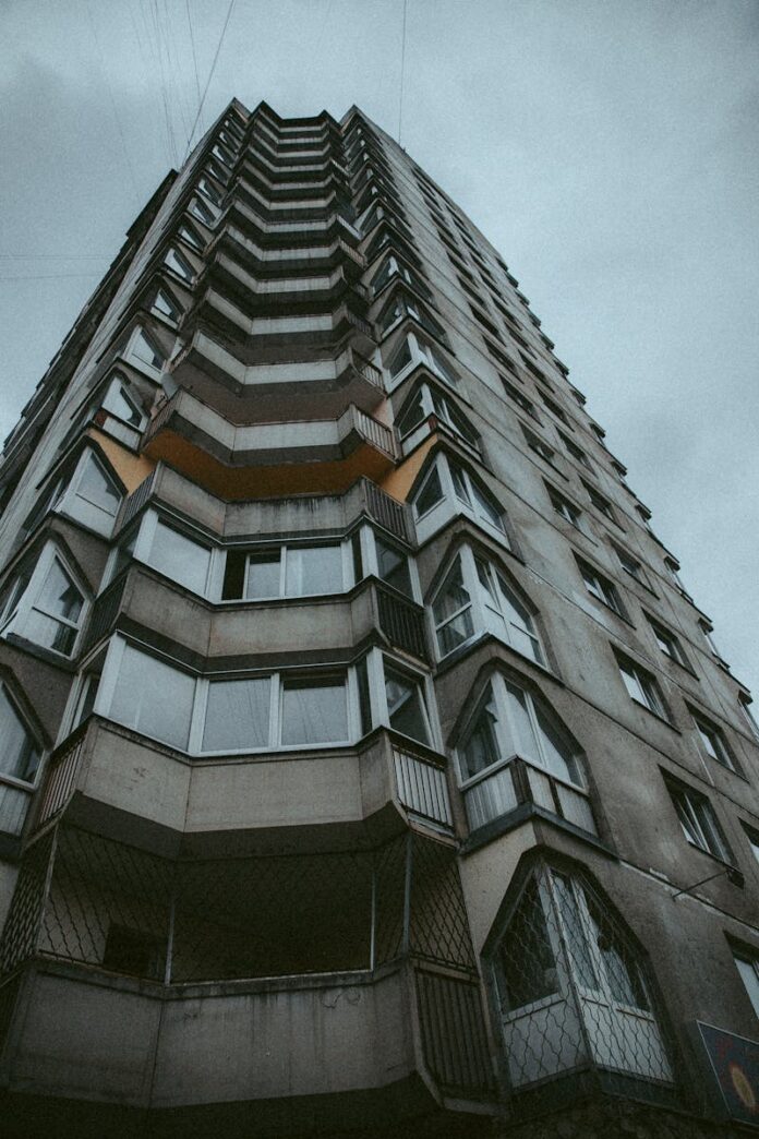 Low-angle view of a tall residential building under grey cloudy skies, showcasing urban architecture.